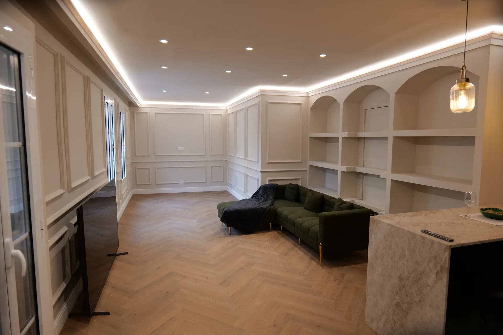 Séjour rénové d’un appartement à Avignon intra-muros : moulures, parquet en bâtons rompus, corniche lumineuse et bibliothèque en arches