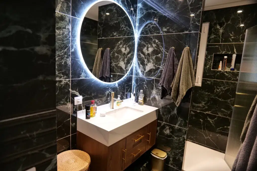 Salle de bain effet marbre noir veiné avec miroir rond rétroéclairé et meuble vasque